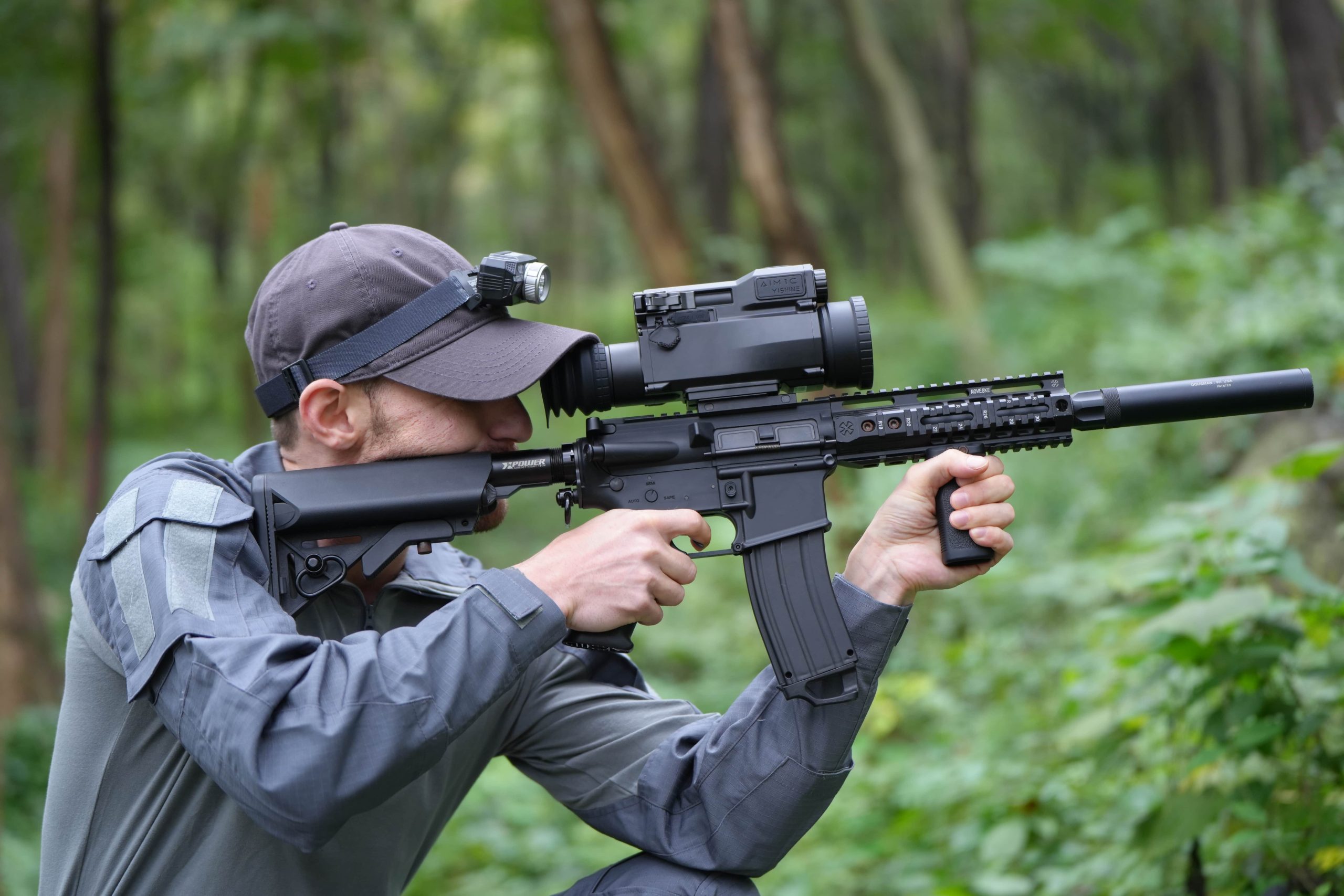 The man is using a monocular to aim at his prey, with a jungle behind him